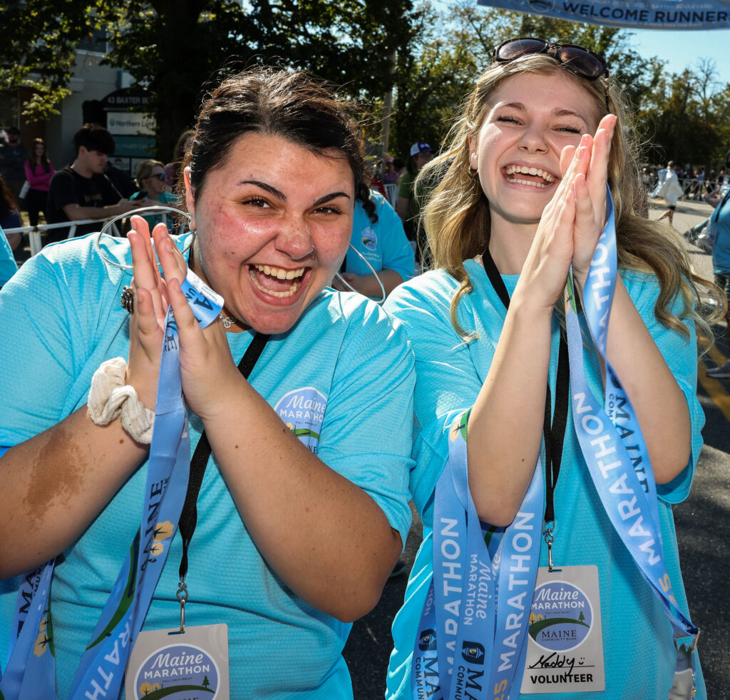 Happy looking volunteers clap while holding medals to give to runners